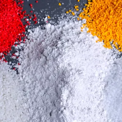 Close up of pile of bright white nepheline syenite mineral next to piles of orange and red colored masterbatch pellets for use in plastics production.