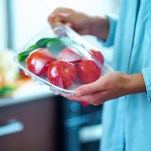 Woman holding a plate of plastic wrapped tomatoes