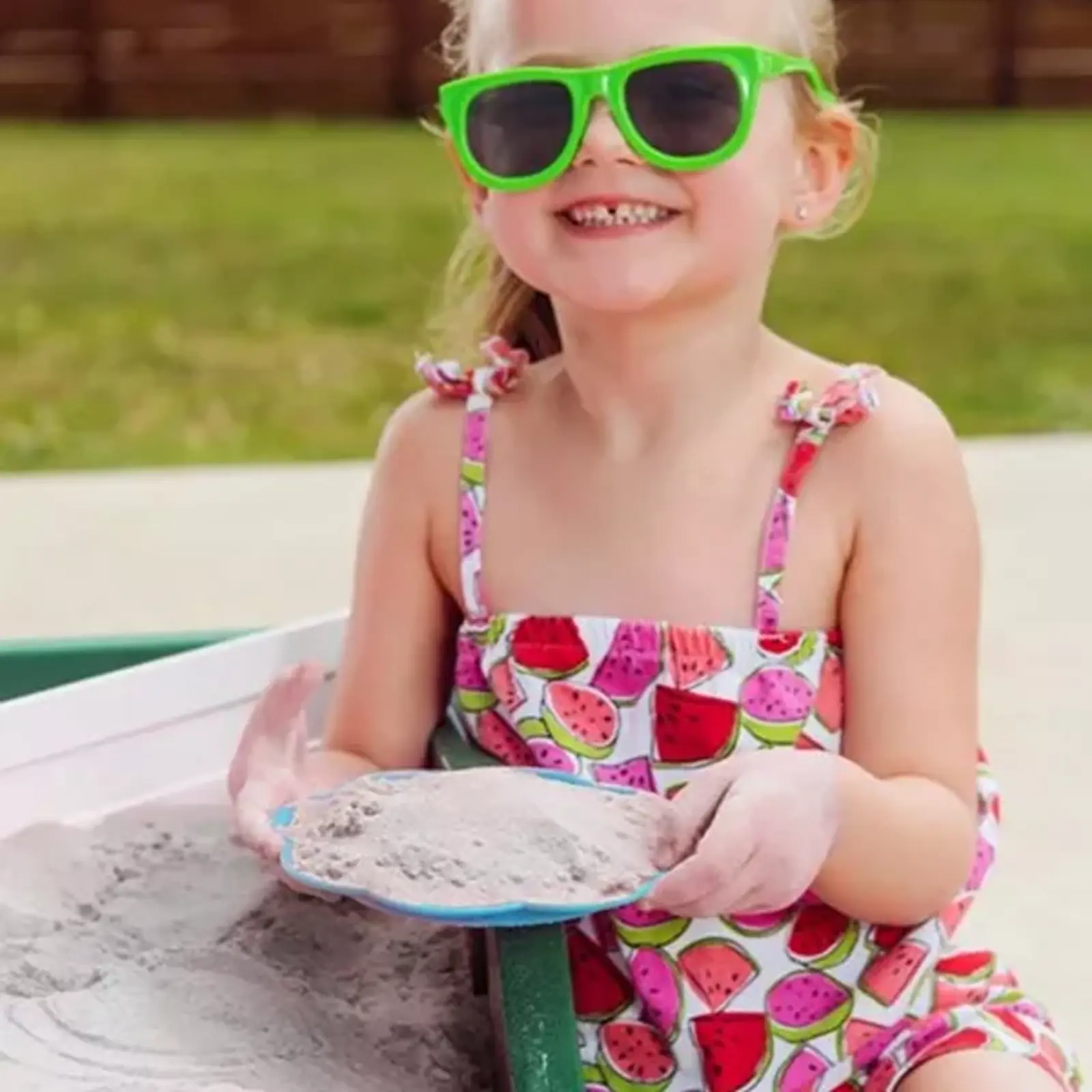 Young girl child happily playing with clean, non-toxic, white Premium PLAYSAND in outdoor sand box with toys.