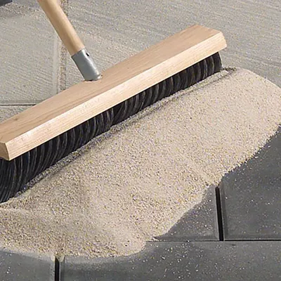 Broom sweeping high quality ACCEL polymeric sand into joints between pavers, stones, flagstones for both professional and DIY use by landscapers and home owners.